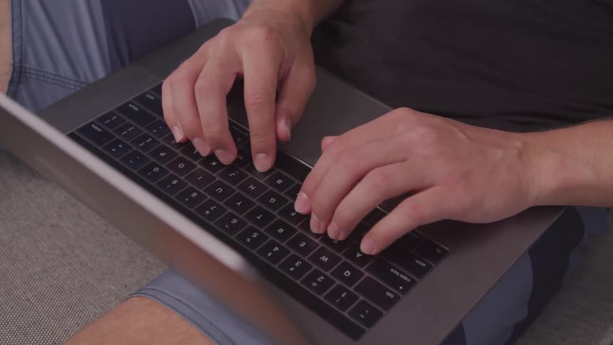 A man sits with his laptop in his lap and types