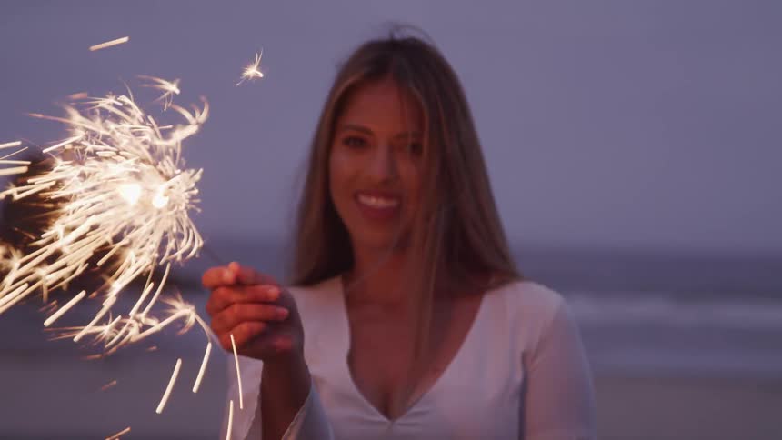 A woman standing on the beach smiling with a sparkler in her hand