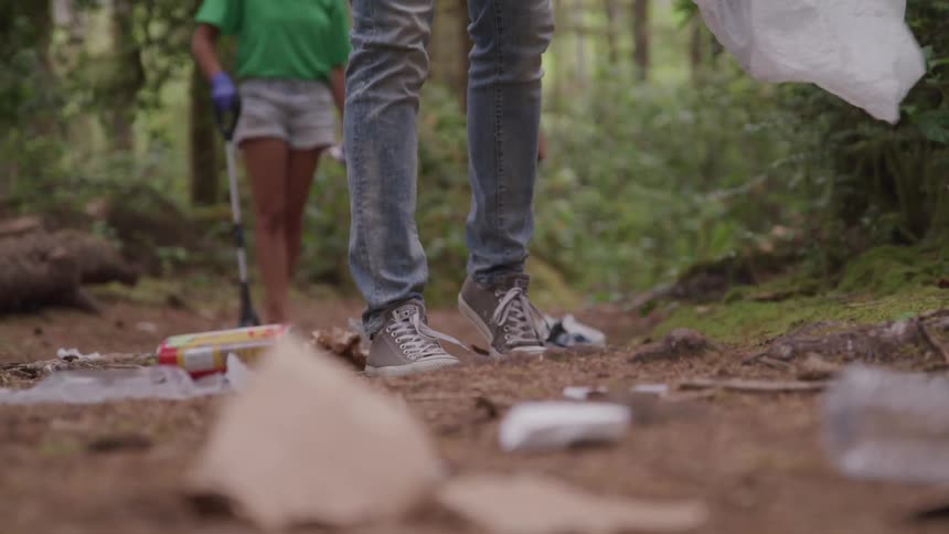 Two people are slowly making their way along an outdoor trail while picking up trash with long trash pricker tools
