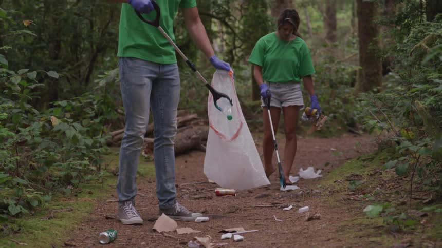 Couple cleaning up a trail picking up litter in the forest