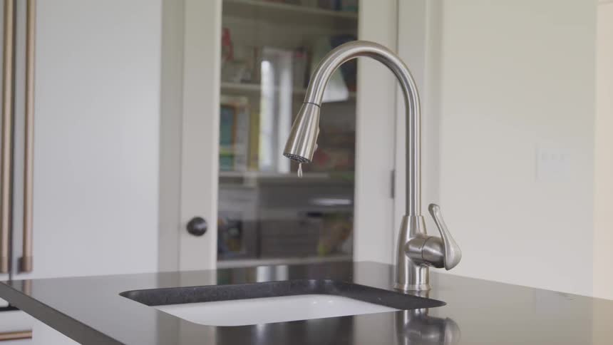 A chrome faucet drips into a kitchen sink