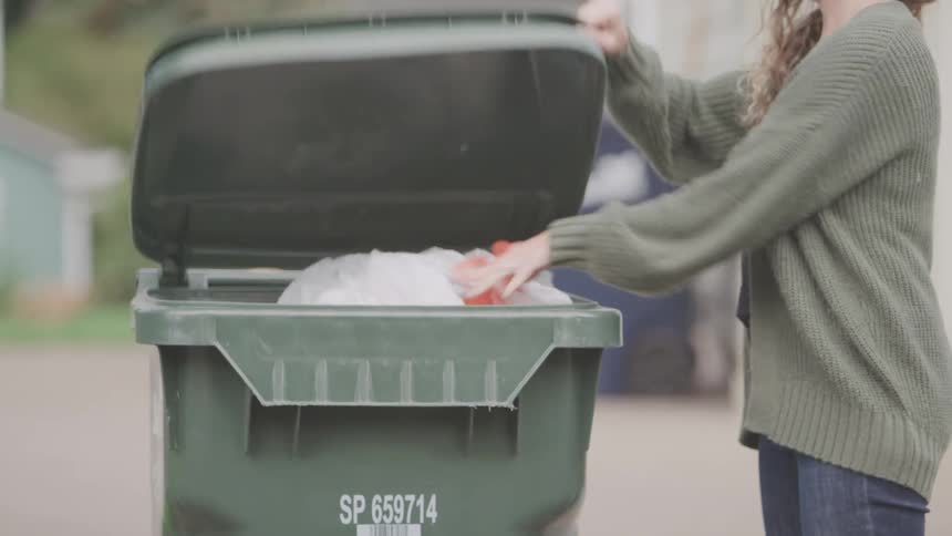 A woman throws a bag of trash in to a garbage can