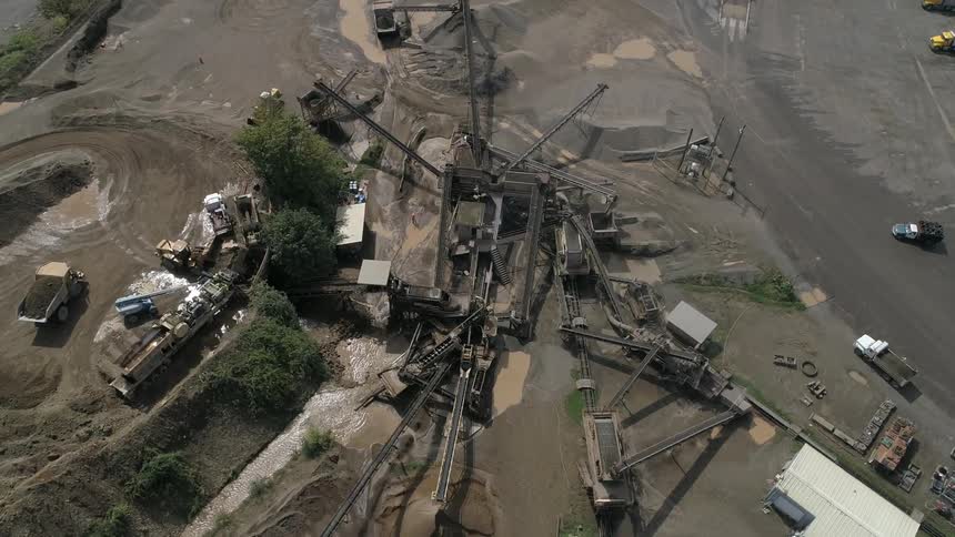 Several trucks are operating at an industrial site with many conveyors