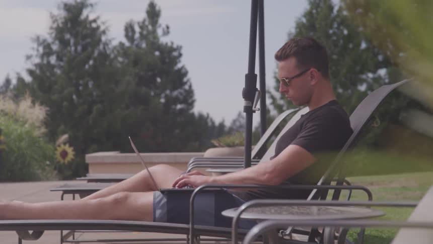 Man relaxing on a lounge chair typing on his laptop