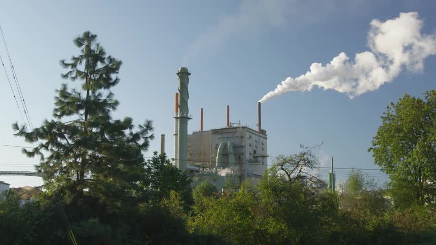 White smoke billows out from building smoke stacks into a blue sky
