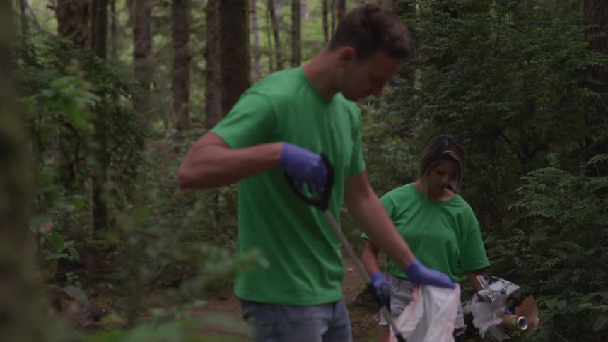 A man and woman pick up trash in a forest
