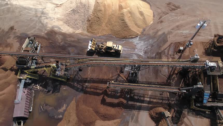 A bulldozer travels on sand near stone crushing equipment in a gravel pit