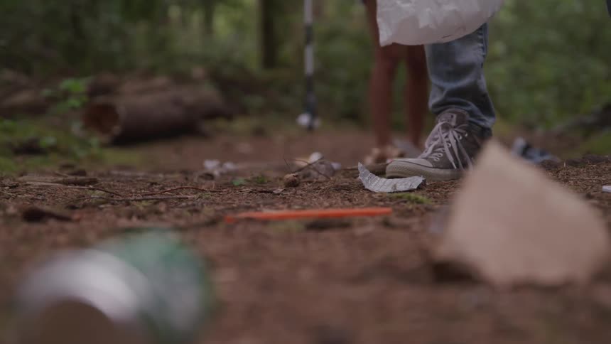 The legs and sneakered feet of people picking up trash in the woods