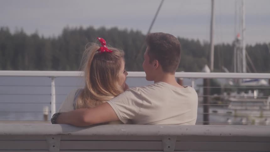 A man kisses his girlfriend on the forehead as they sit in front of the water