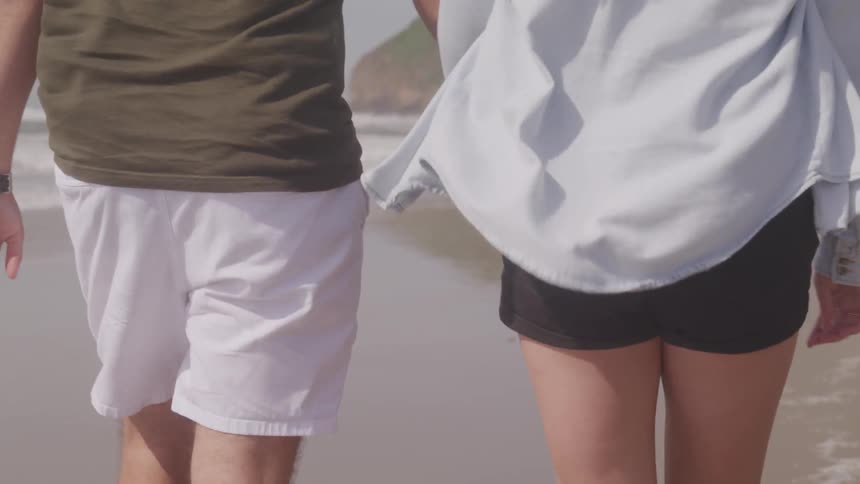 A man and woman walk along the beach holding hands