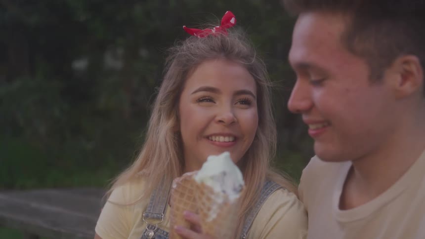 Blonde girl and boy looking and smiling at each other eat ice cream at dusk