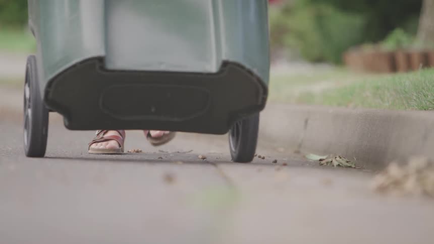 A woman pushes a garbage can along the sidewalk