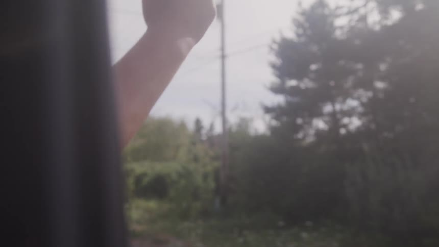 A person sticks their arm out of the passenger side window as the car drives down the road