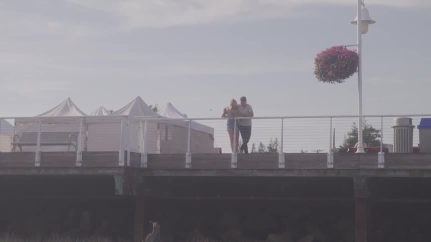A young couple stands against a railing and looks below