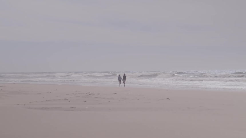 A man and woman walk along a beach