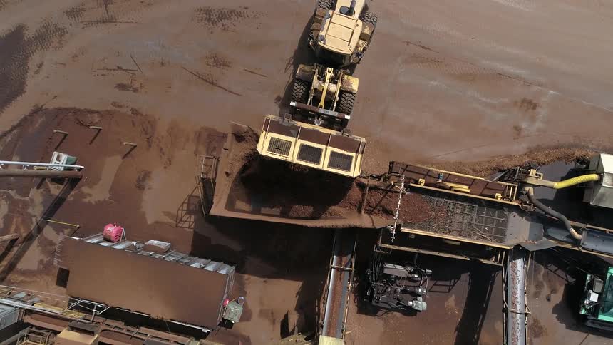 A large industrial vehicle is unloading soil into a enormous sifter at a processing facility