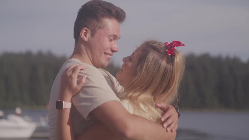 A man and woman hug and then kiss while standing outside in the sunshine