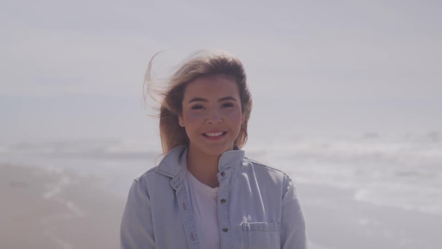 A woman stands on the beach with the wind blowing through her hair