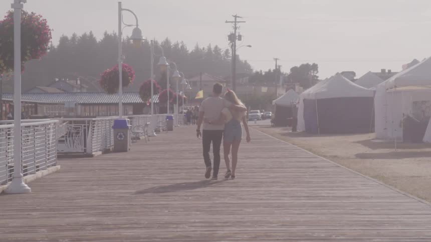Blonde girl and boy holding each other stroll along on the promenade on a sunny day