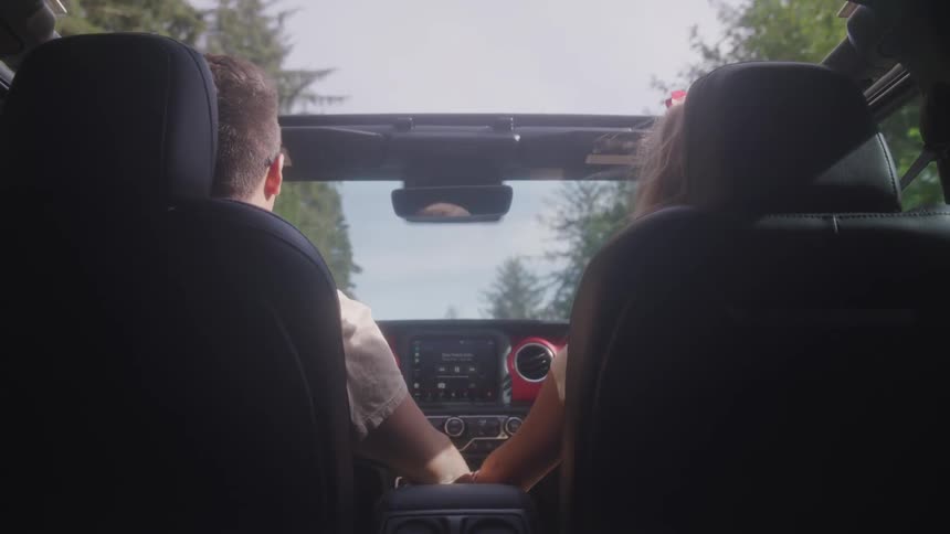 A male drives a convertible and a female sits in the passenger seat