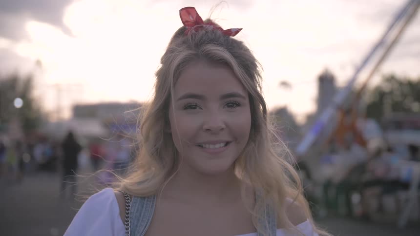A young blonde woman stands outside and smiles