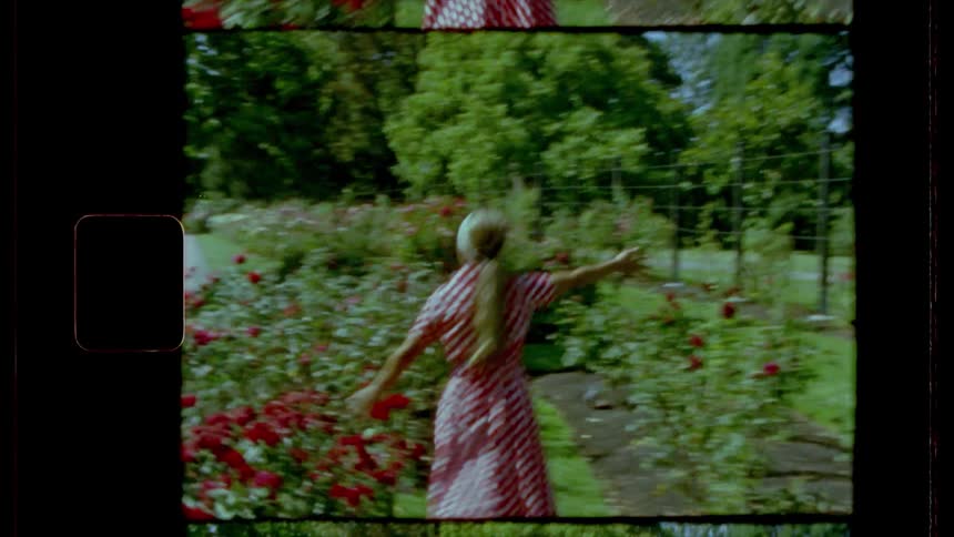 A woman in a rose garden jumping up and down turning and skipping forward