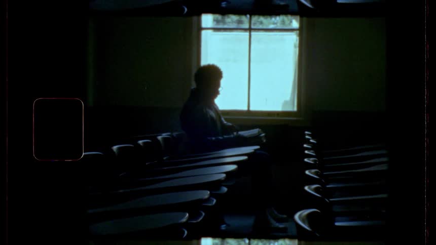 A man is sitting alone at a desk near a window in a dark room
