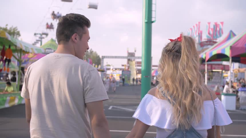 Two teens walk through an amusement park together holding hands