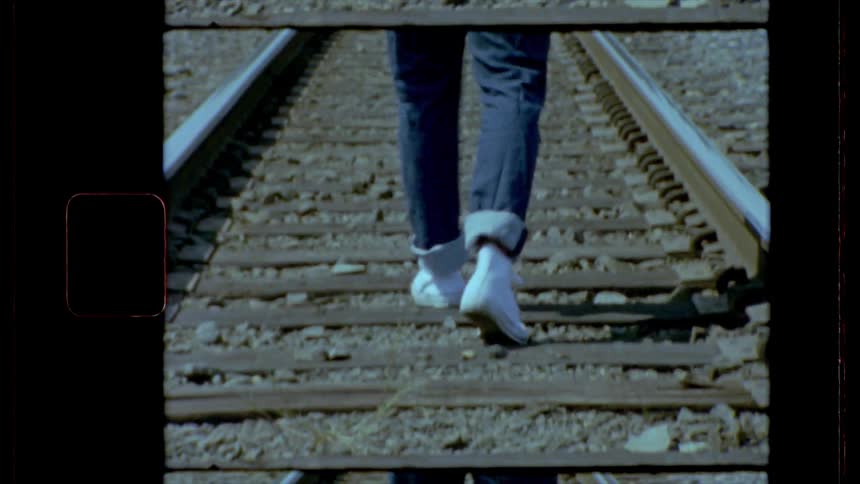 Legs of a man wearing jeans walking on railroad tracks