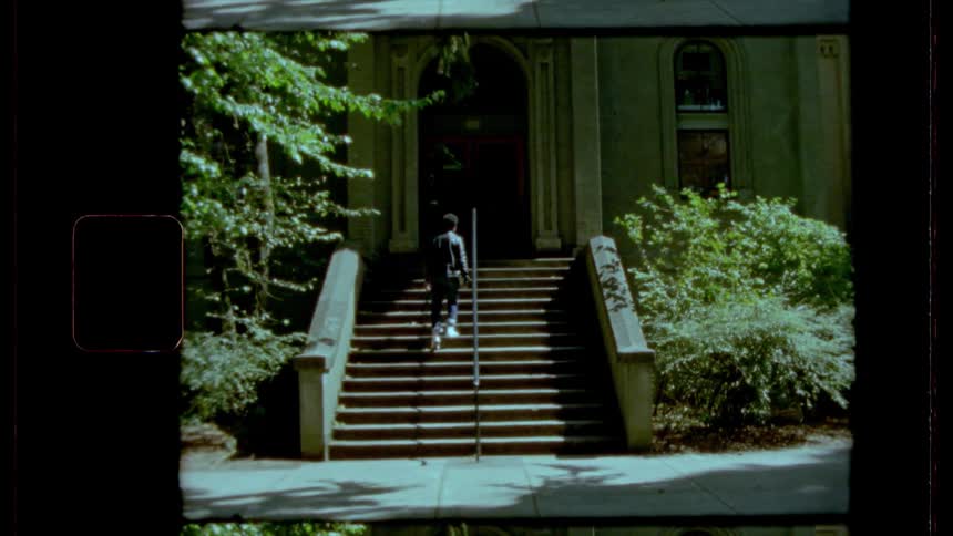 A man walks up a staircase outdoors that leads to a large building