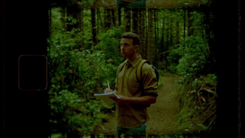 Man standing on the forest track looks up in the sky and takes notes in the woods