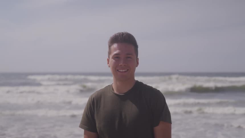 A man smiles as he stands in front of crashing waves in the ocean