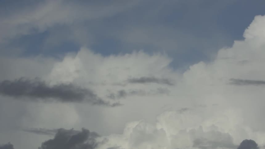 Gray clouds billow and move past white clouds in a blue sky