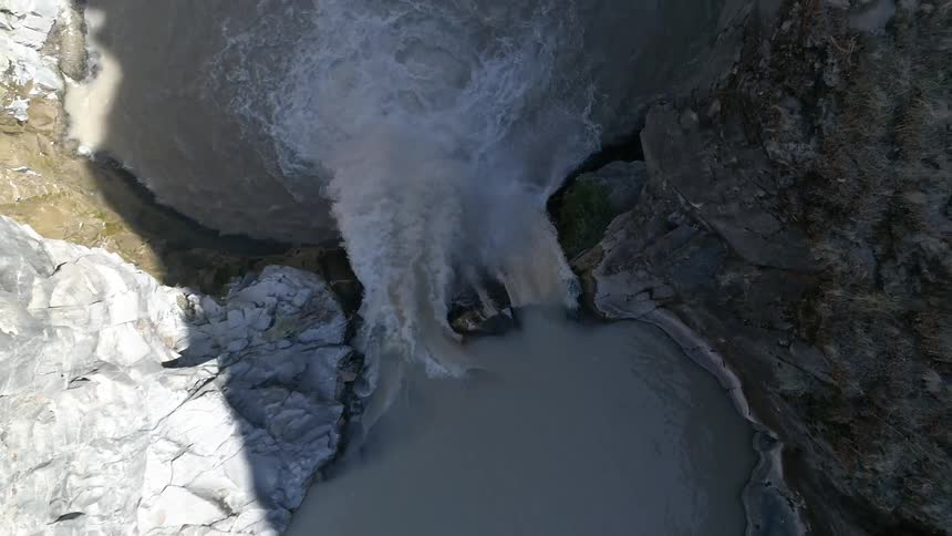 A muddy waterfall rushes and flows into a basin below