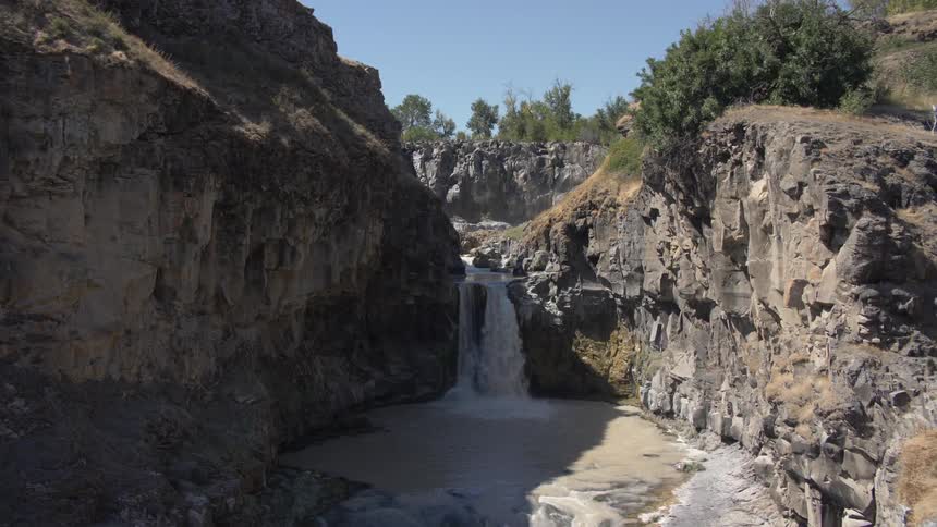 A fast flowing waterfall spills over a rocky wall and pours into a small muddy pool of water below