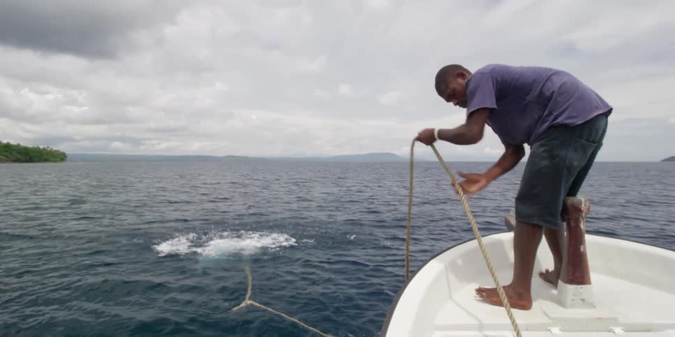 A man on a boat throws an anchor into the water