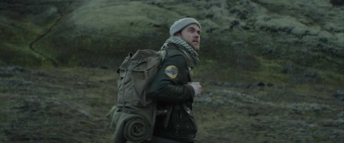 A man with camping gear and a backpack hikes through a hilly terrain