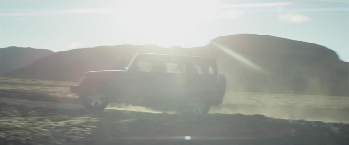 Jeep drives along road past low mountains and wide fields