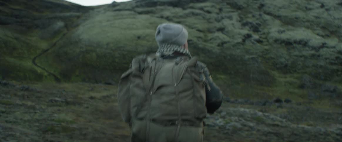A man wearing a large backpack turns and continues hiking up a rocky slope