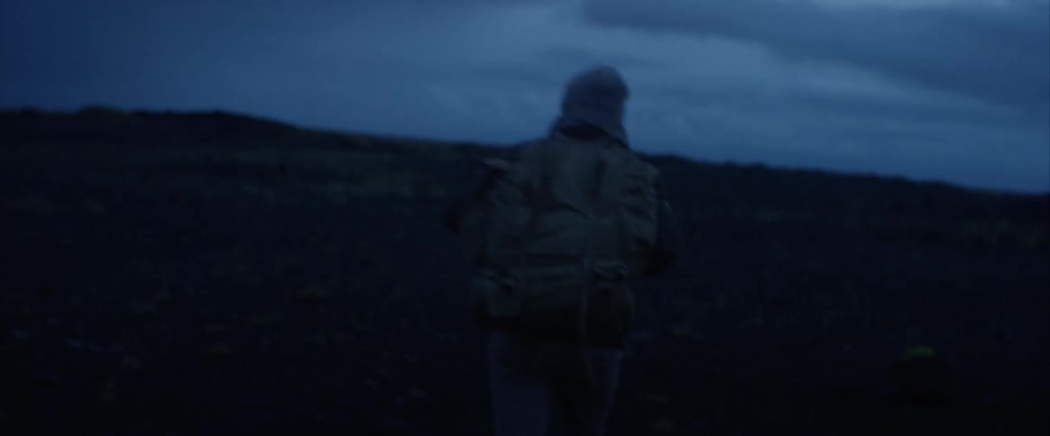 A man with a backpack walking with the sky in the background
