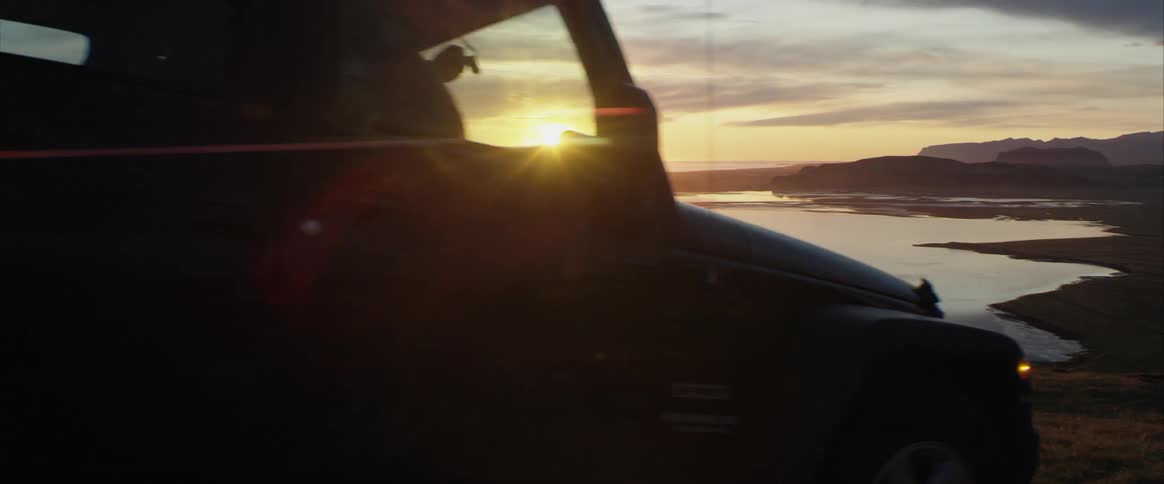 A jeep drives on the beach as the sun rises