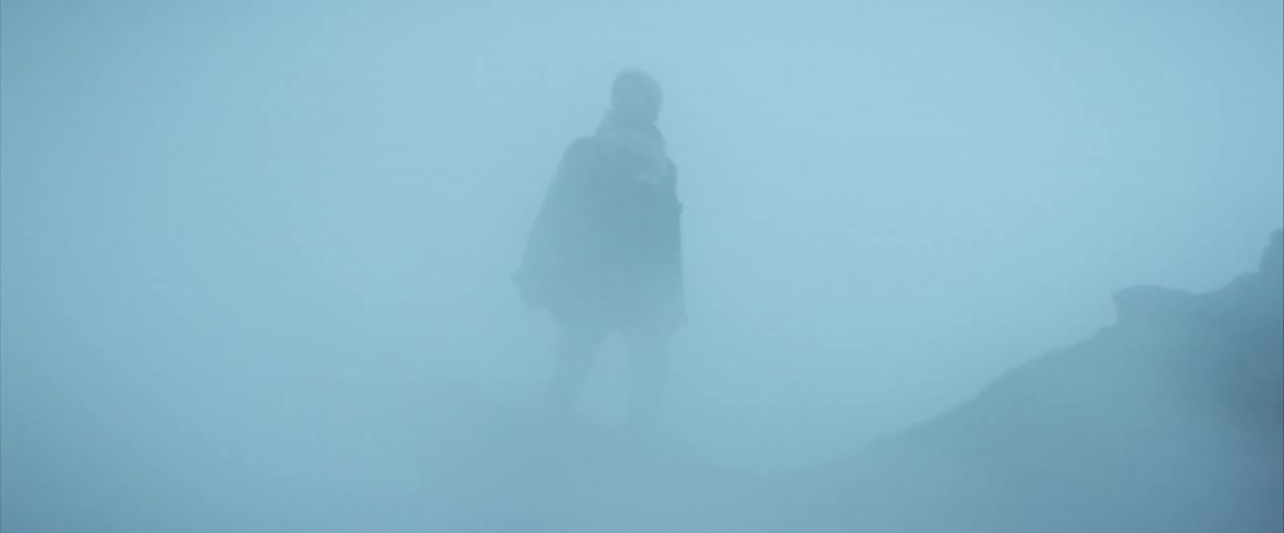 A hiker struggles to cross the terrain as strong wind blows sand all around him