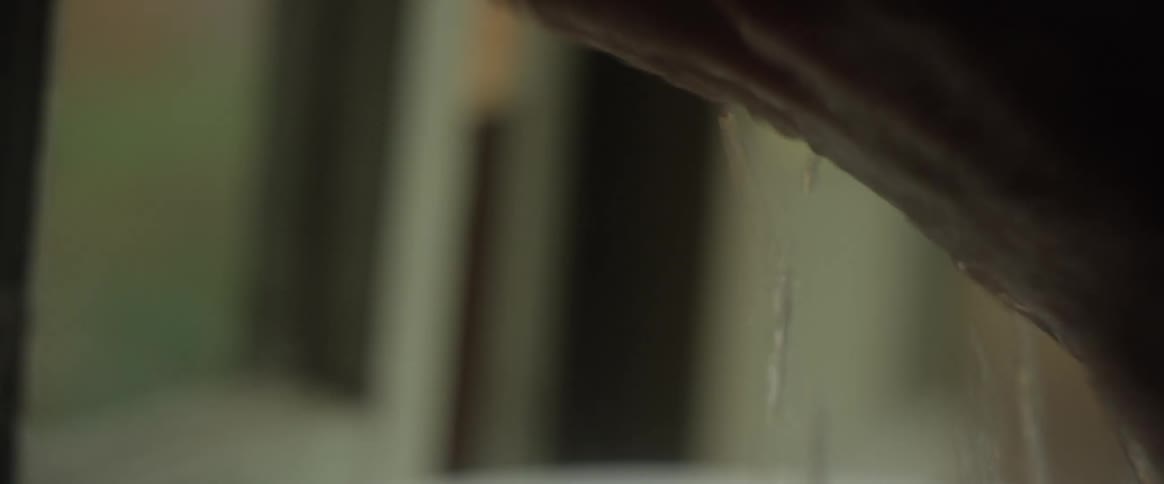 A woman puts her hands in a sink of water and splashes the water on her face