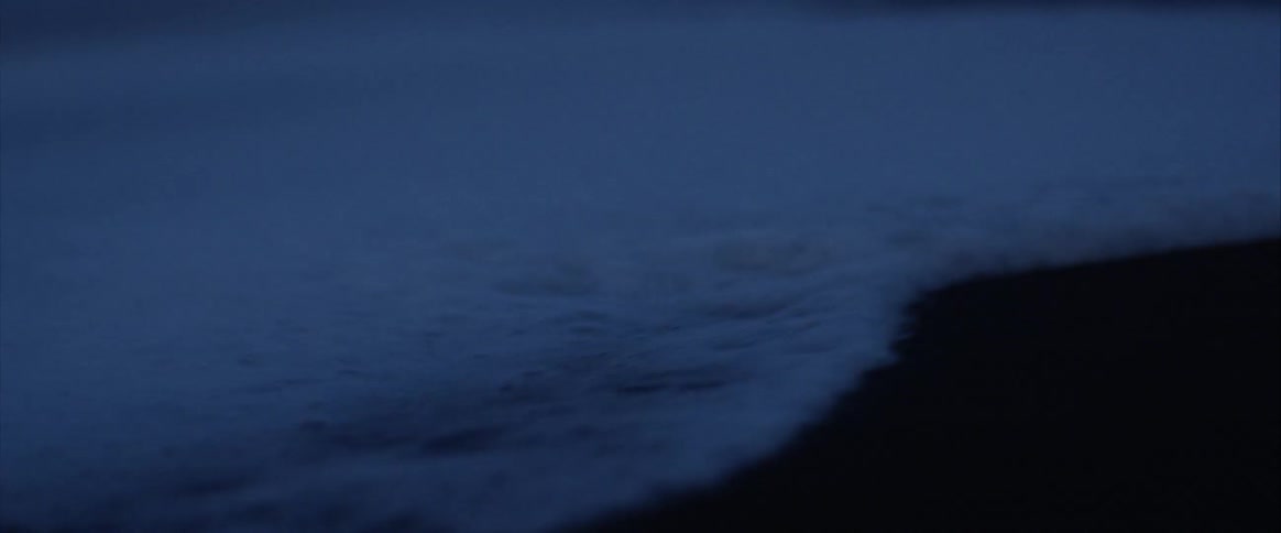 A close up of a wave hitting the beach at night