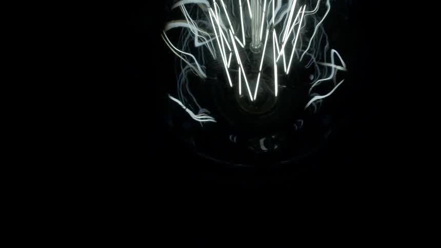 A light bulb with white filament glowing inside with a black background