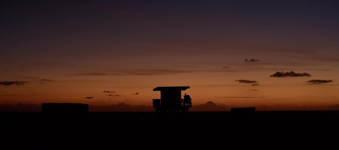 Silhouettes of people standing on a beach hut lifeguard house at sunset