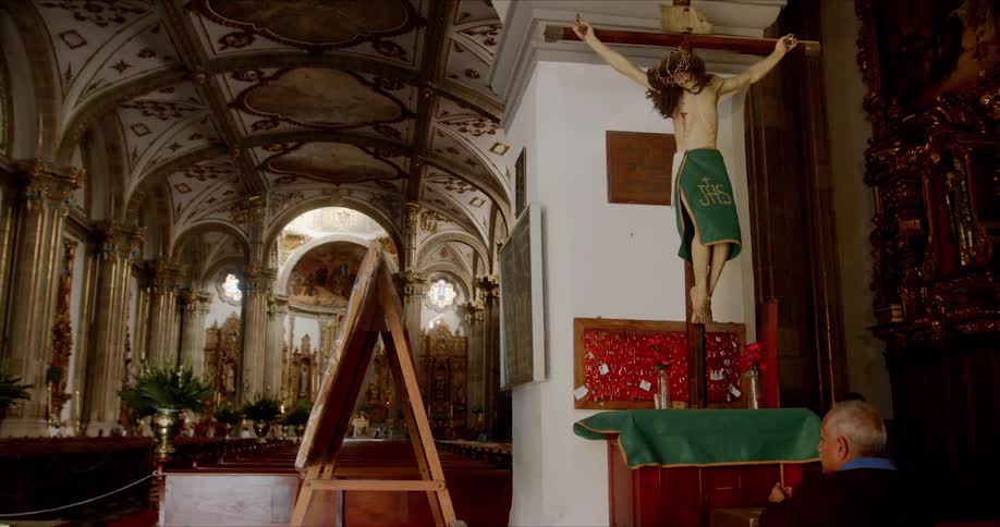 A man prays before a mannequin resembling jesus inside an ornate church