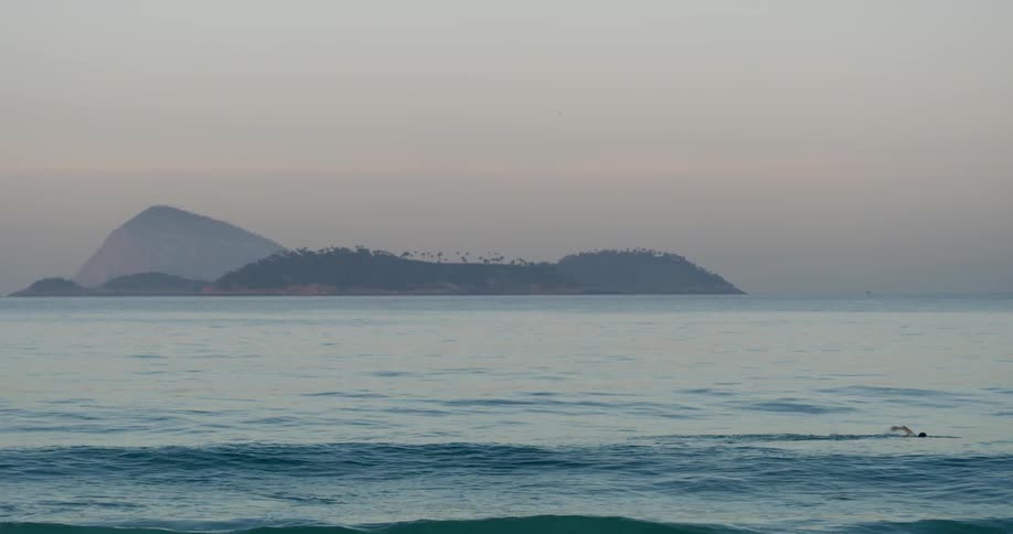 A person swims in the ocean at sunrise with islands visible in the distance