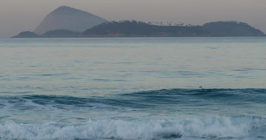 A person swims in the ocean waves alone at sunrise