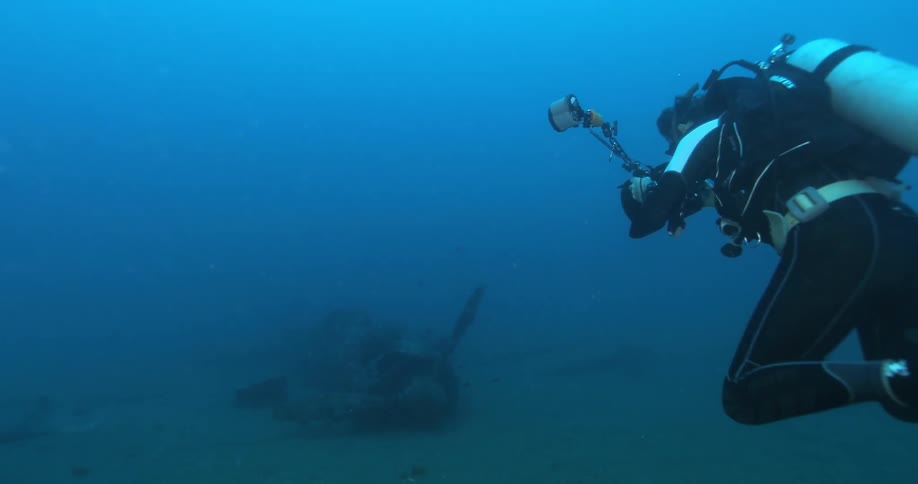 A scuba diver with photographic gear swims near some airplane wreckage